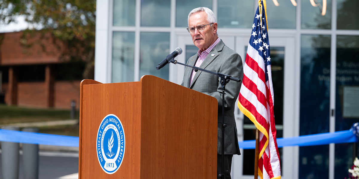 Ohio Lt. Gov. Jim Tressell stands at a podium decorated with the NEOMED seal