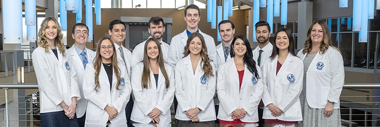 Fourteen students stand in two rows in white coats.