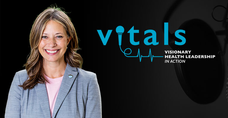 A smiling physician in a suitcoat against a dark background.