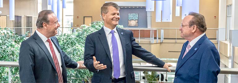 Three men in coats and ties talk in the atrium at NEOMED.