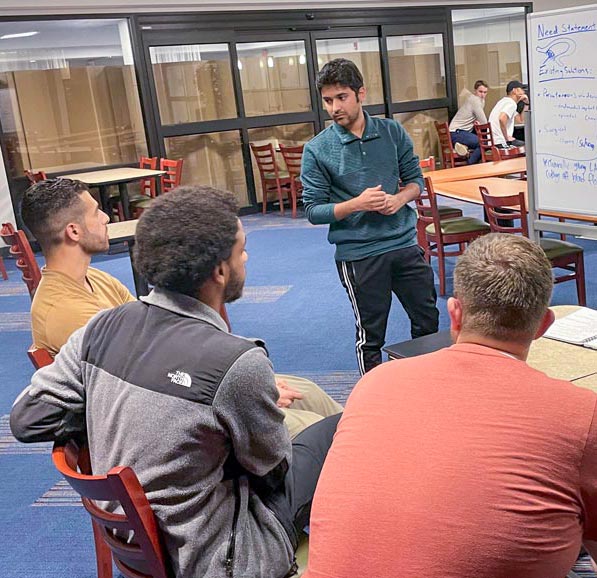 A man stands at a whiteboard taking suggestions from one of three partners.