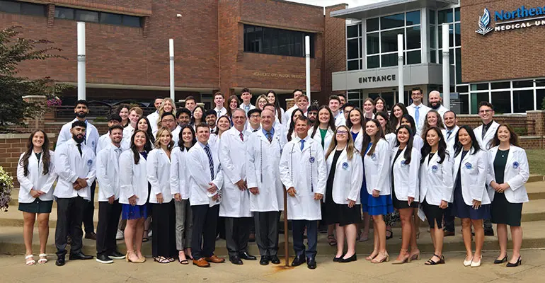 The inaugural class of students in the Bitonte College of Dentistry stands on the steps outside of NEOMED in their white coats.