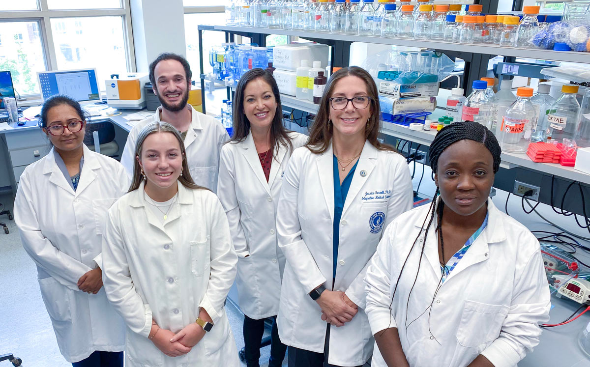 A NEOMED researcher stands with her research associates. They are all in white coats.