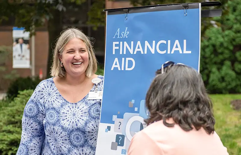 A financial aid specialist talks with a student at an outdoor campus event.