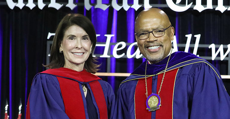 Nancy Gantt accepts an award on a stage standing next to a man in ragalia.