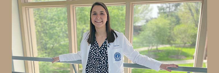 A woman in a white coat with a window in the background.