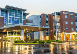 The main entrance to NEOMED on a rainy evening, with the building reflected in puddles.