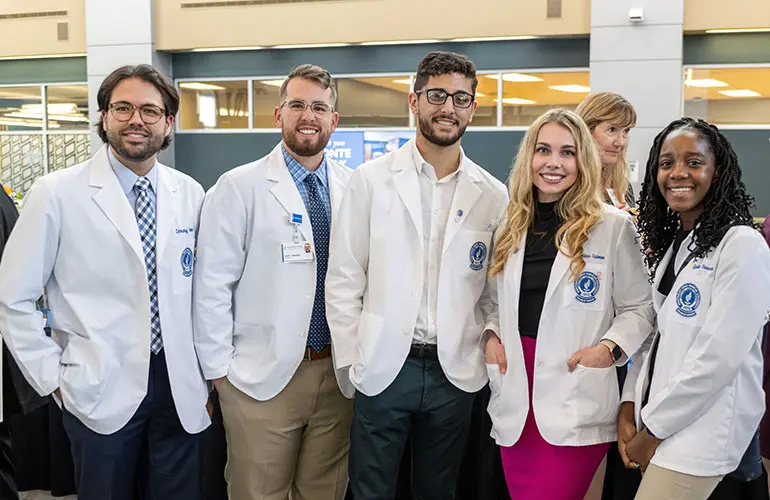 Five NEOMED students in white coats at a campus event.