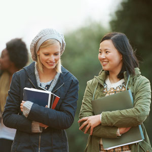 Two women dressed in sweaters chat as they cross campus on a fall afternoon.