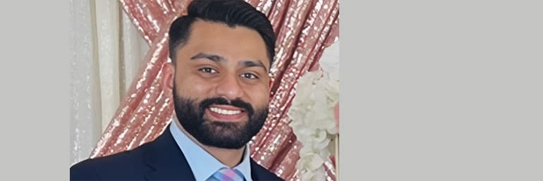 A spring graduate of NEOMED stands before a curtain for a portrait.