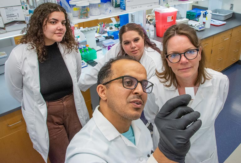 Four lab researchers in white coats look at a slide.