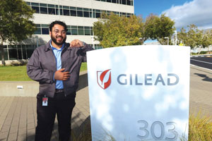 A man stands outdoors, leading next to a business sign that reads Gilead.