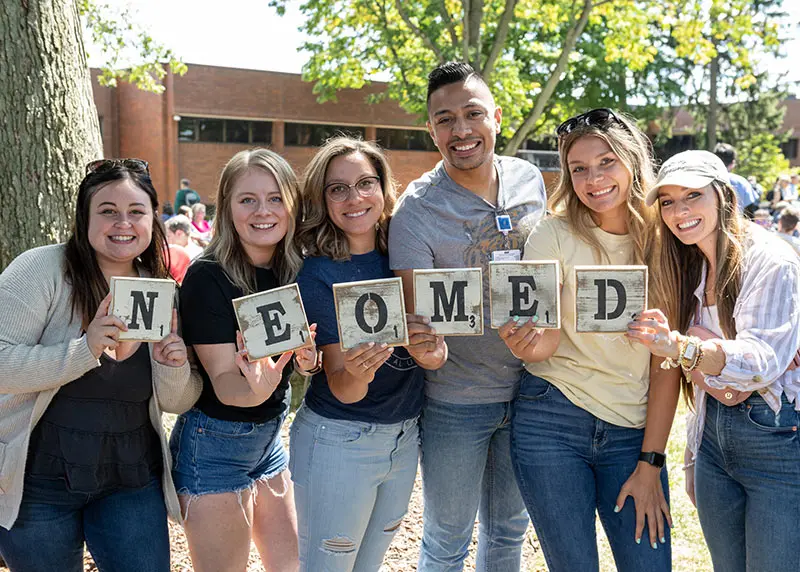 Two people in surgical attire smile for a photo while holding medical fluid bags in a clinical setting.