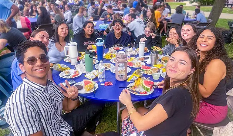 Students sit around a large circular table in a courtyard at NEOMED during a campus picnic.