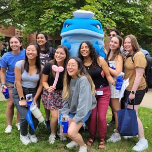 College students stand around someone in a whale costume, which is a mascot.