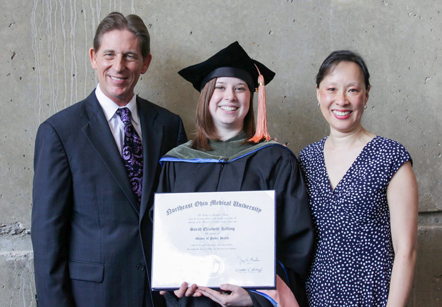 A man and woman standing on either side of a woman holding a diploma.