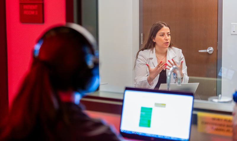 A student doctor gestures as she speaks with a patient actor in a simulation lab at NEOMED.