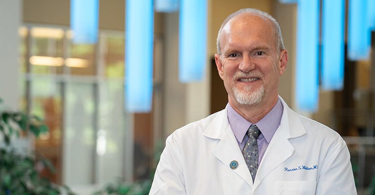 A doctor in a white coat stands in the atrium at NEOMED.