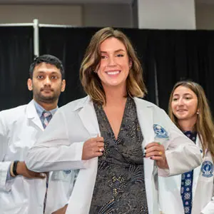 A smiling medicine student wears her white coat for the first time.