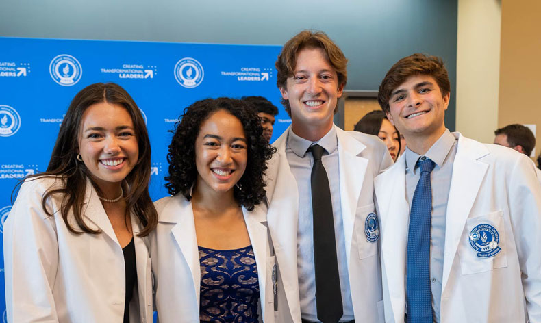 Four new students in white coats pose for a photos after their White Coat Ceremony at NEOMED