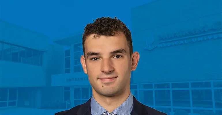 A man in a coat and tie against a background that shows the front of the University.
